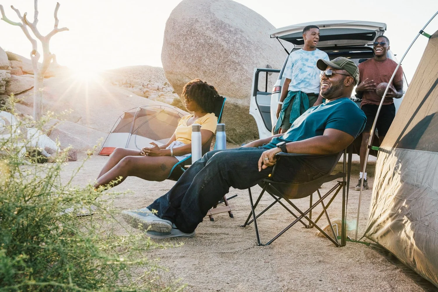 Family relaxing in camp chairs beside the Rivian
